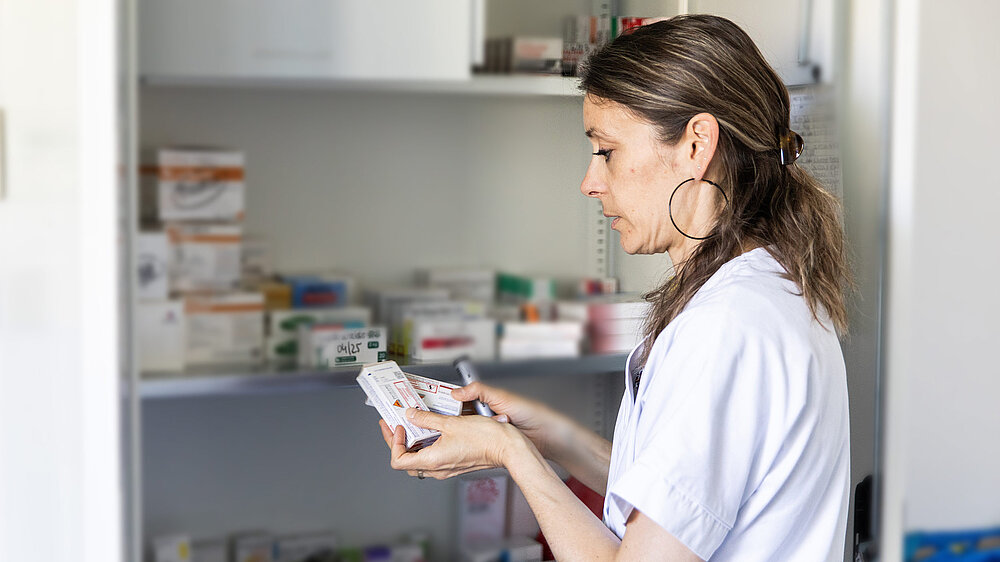 Professionnelle de santé tenant un médicament devant l'armoire à pharmacie